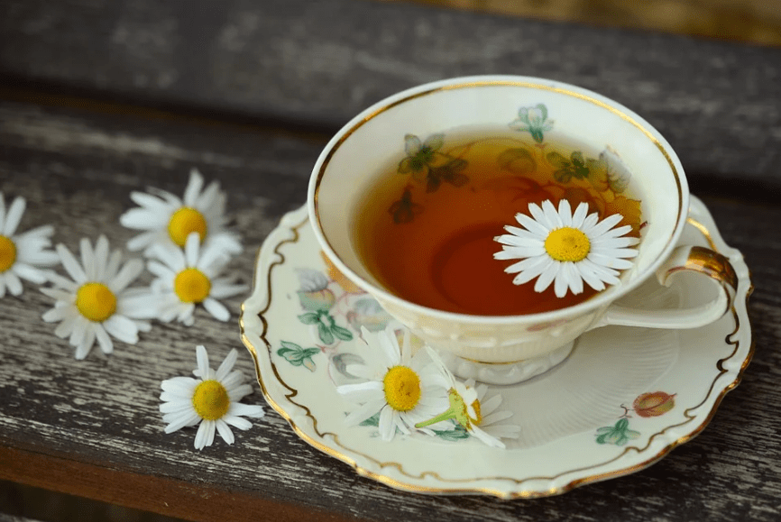 a cup of chamomile tea, flowers, porcelain tea set, wood
