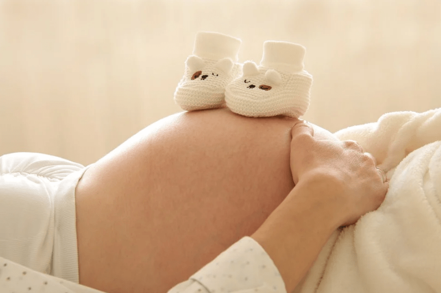 big baby bump, two white knitted shoes on the mother’s belly, girl wearing white clothes
