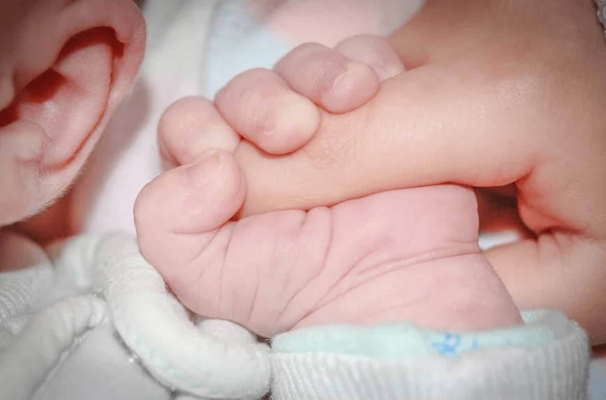 ear of a baby, baby holding the finger, white baby clothes