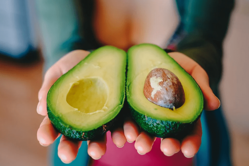 avocado fruit sliced into half, two hands holding the fruit, brown avocado seed
