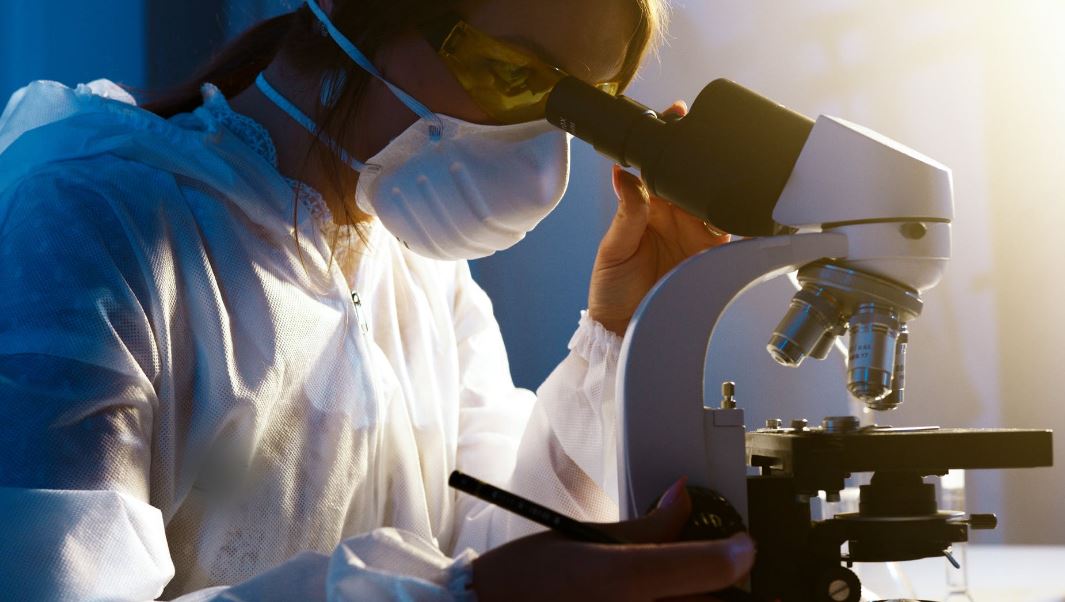 a woman in a laboratory, looking through a microscope